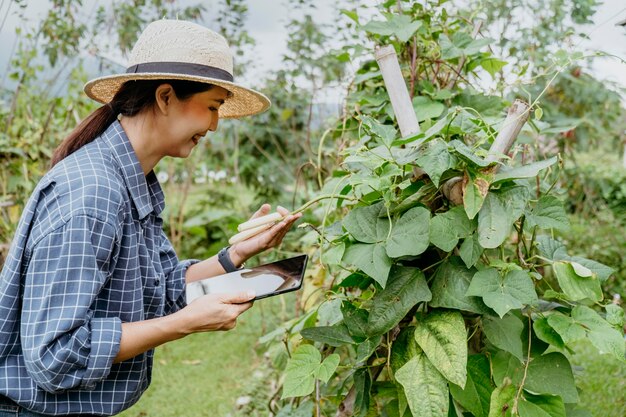 Mujer asiática de lado estudiando diferentes plantas con una tableta