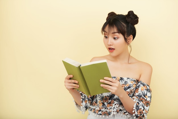 Mujer asiática con libro abierto y mirándolo con expresión de incredulidad en la cara