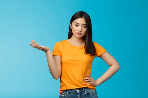 Mujer asiática mandona ignorante de alto nivel, mirada consternada arrogante, actuar esnob quejándose del mal servicio, levantar la mano con total incredulidad, no puedo soportar tonterías, estar de pie molesto fondo azul