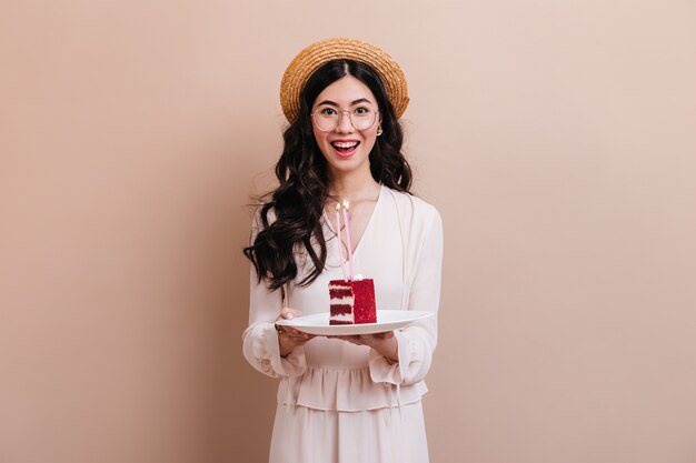 Mujer asiática mirando a la cámara con una sonrisa. Feliz mujer japonesa con sombrero de paja con pastel.