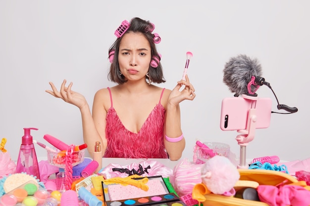 La mujer asiática morena descontento mira con expresión indignada sostiene cepillo cosmético