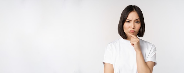 Foto gratuita mujer asiática pensativa mirando a un lado reflexionando sobre hacer suposiciones pensando o eligiendo algo de pie sobre fondo blanco