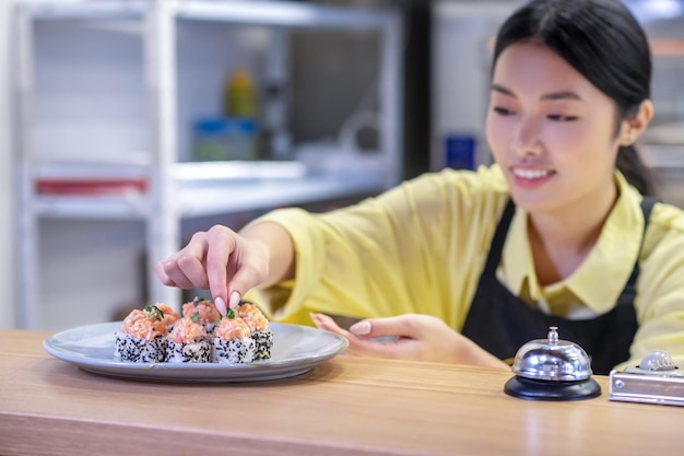 Mujer asiática poniendo sushi en el plato y luciendo inspirada