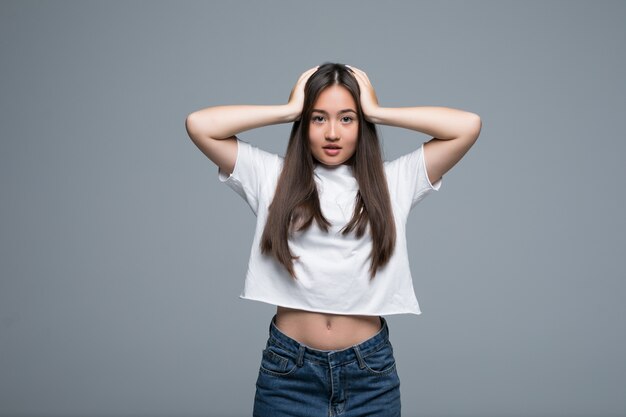 Mujer asiática preocupada en ropa casual cubriendo sus orejas mientras mira lejos sobre fondo gris