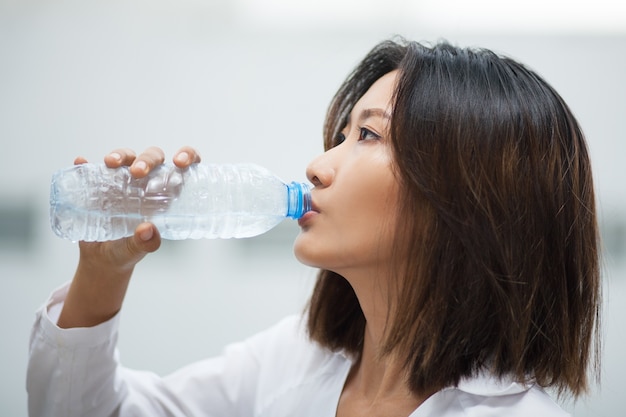 Mujer asiática que bebe agua de la botella plástica
