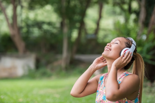 Mujer asiática que escucha la música preferida en los auriculares. Tiempo feliz y relajarse