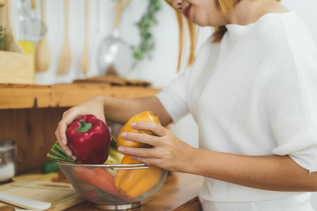 Mujer asiática que hace la comida sana que se coloca feliz sonriendo en la cocina que prepara la ensalada