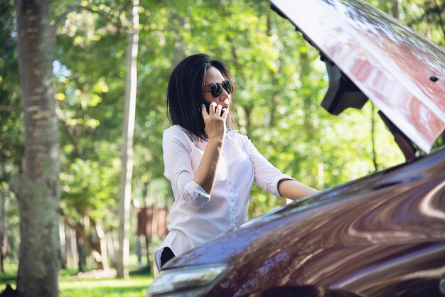 Mujer asiática que llama al reparador o al personal de seguros para arreglar un problema del motor del automóvil en una carretera local