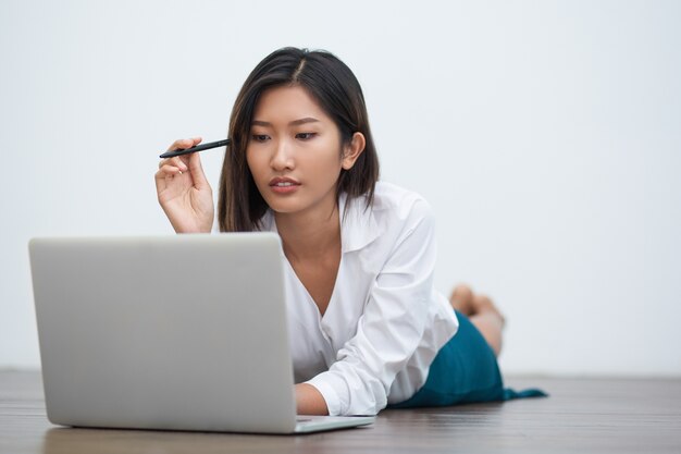 Mujer asiática que miente en el suelo y trabajar en la computadora portátil