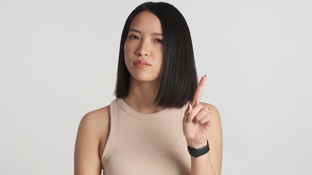 Mujer asiática que parece confiada sin mostrar ningún gesto a la cámara sobre fondo blanco Expresión en desacuerdo