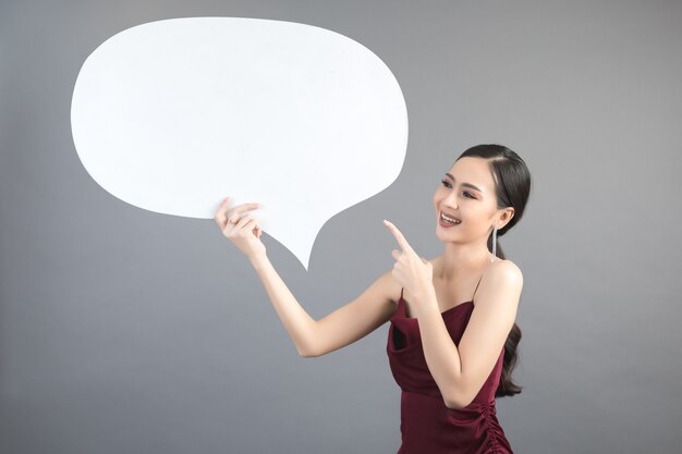 Mujer asiática que sostiene y que mira para arriba a la burbuja del discurso con el espacio vacío para el texto