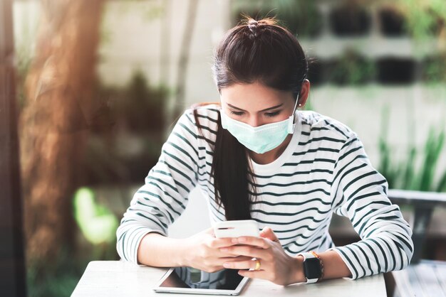 Mujer asiática que trabaja en una computadora portátil mientras usa una máscara médica en el espacio de trabajo conjunto Nuevo estilo de vida normal Distanciamiento social