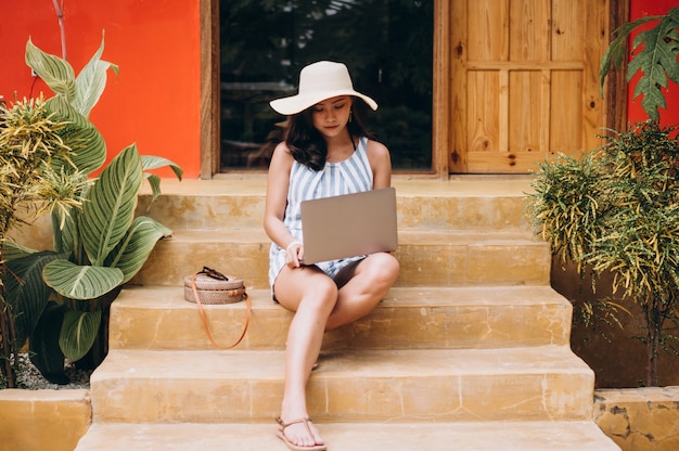 Mujer asiática que trabaja en la computadora portátil en vacaciones y sentado en las escaleras