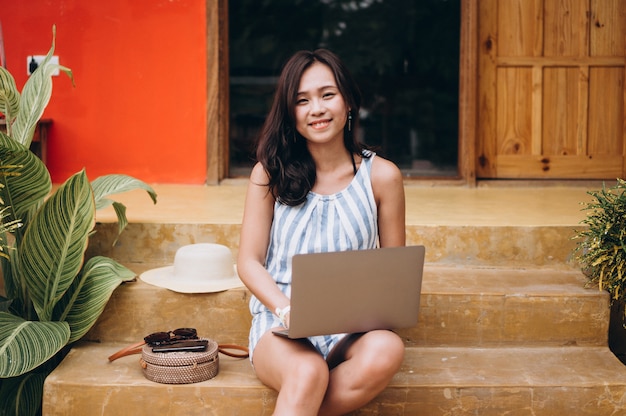 Mujer asiática que trabaja en la computadora portátil en vacaciones y sentado en las escaleras