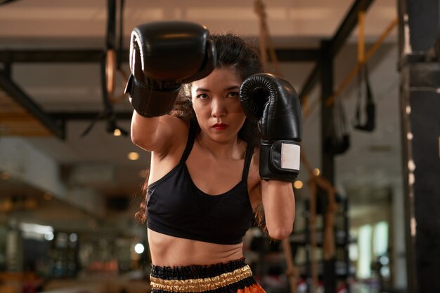 Mujer asiática recortada entrenando en guantes de boxeo en la práctica de Muay Thai