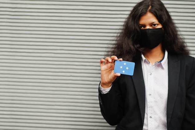 Foto gratuita mujer asiática con ropa formal y máscara protectora negra sostiene la bandera de micronesia a mano contra el fondo gris coronavirus en el concepto de país