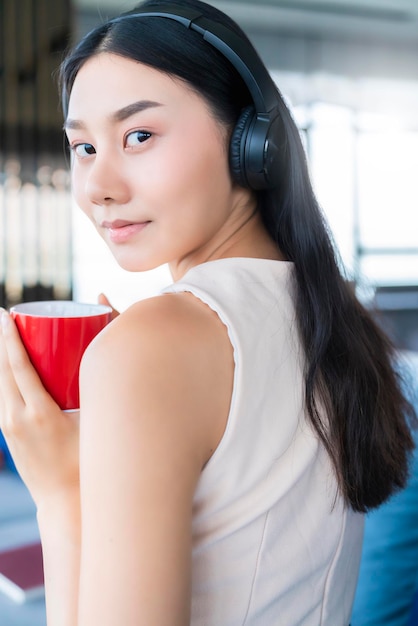 Mujer asiática con ropa de trabajo informal tómese un descanso con café y una revista en el sofá en el fondo de la casa de la sala de estar