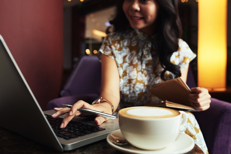 Foto gratuito mujer asiática sentada en la cafetería y trabajando con el portátil y una taza de capuchino en la mesa