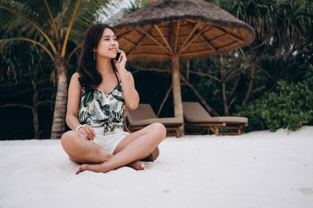 Mujer asiática sentada en la playa y usando el teléfono