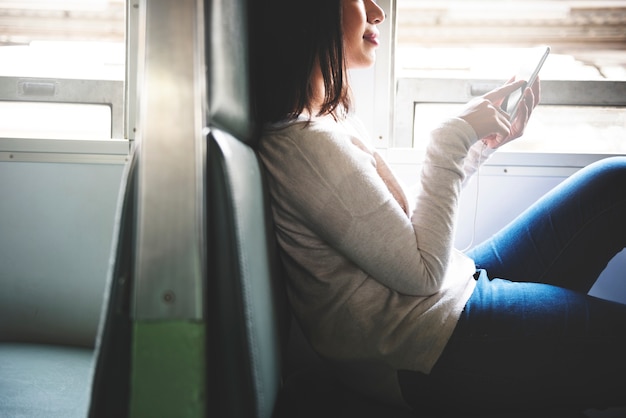 Mujer asiática sentada en un tren usando teléfono móvil