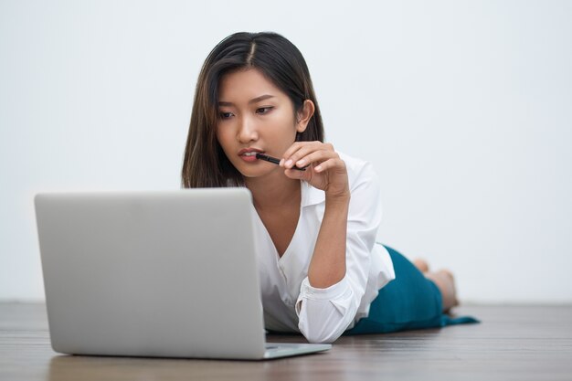 Mujer asiática seria que trabaja en la computadora portátil en el piso