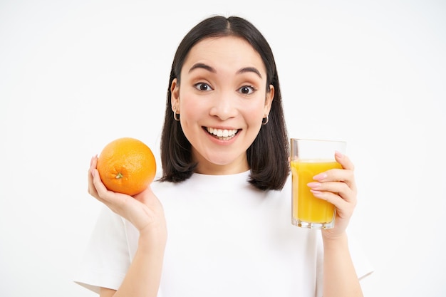 Mujer asiática sonriente bebe jugo de naranja fresco y sostiene fruta en la mano lleva una vida activa y saludable