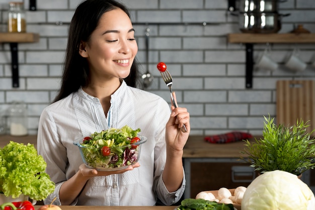 Mujer asiática sonriente con la ensalada sana en cocina