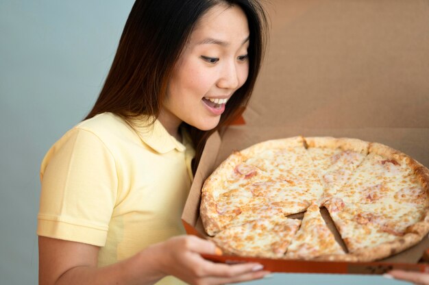 Mujer asiática sonriente mirando una deliciosa pizza