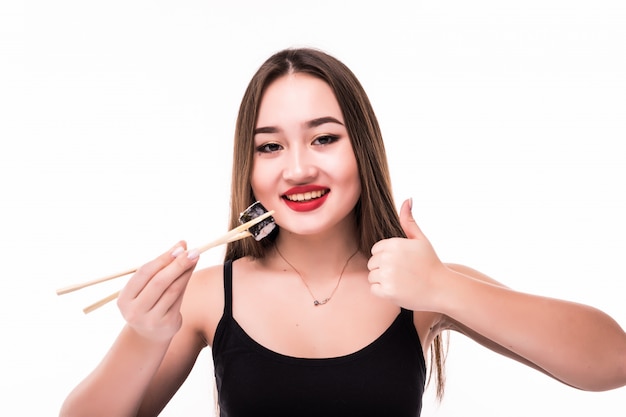 La mujer asiática sonriente prueba los rollos de sushi muestra los pulgares encima de la muestra aislada