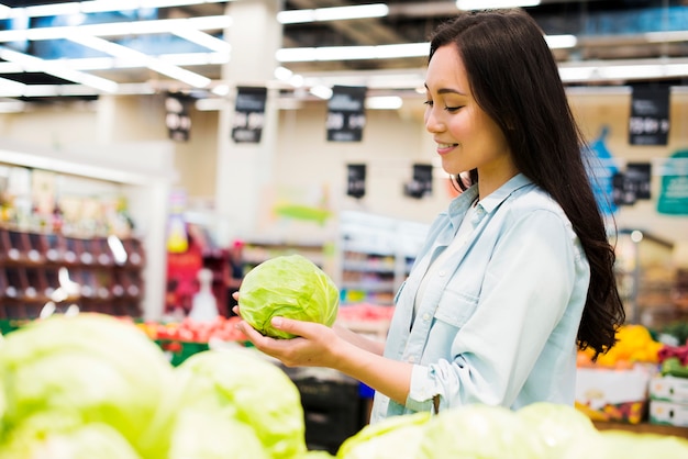 Mujer asiática sonriente que elige la col en mercado