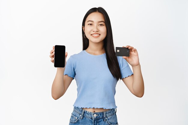 Mujer asiática sonriente que muestra la pantalla del teléfono móvil con el concepto de tarjeta de crédito de compras y pedidos en línea