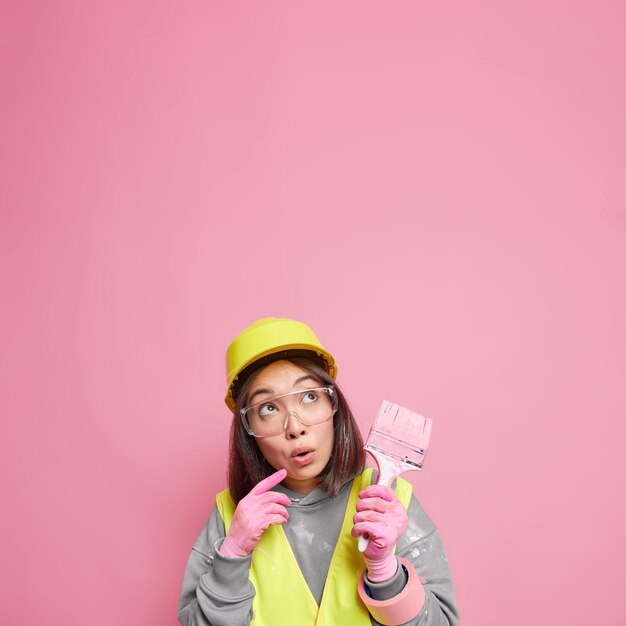 Mujer asiática sorprendida concentrada piensa en la remodelación del apartamento sostiene un pincel de pintura