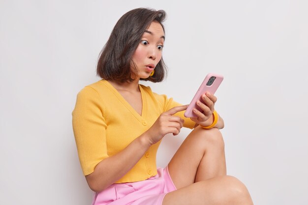 Una mujer asiática sorprendida y sorprendida mira fijamente al teléfono inteligente.