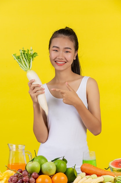 Mujer asiática Sostén el rábano con la mano derecha y sobre la mesa hay muchas frutas.