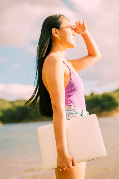 Mujer asiática sosteniendo portátil y mirando al sol
