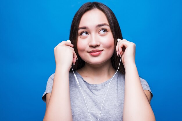 Mujer asiática usando audífonos y escuchando música aislado en una pared azul