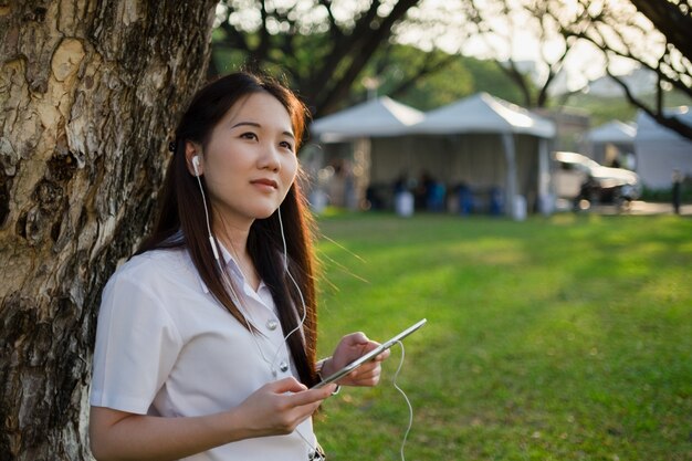 Mujer asiática usando la tableta y escuchando la música