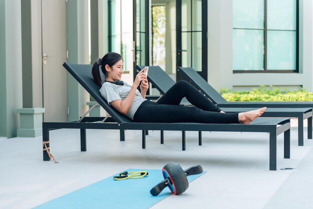 Mujer asiática usando teléfono inteligente y relajándose después del entrenamiento