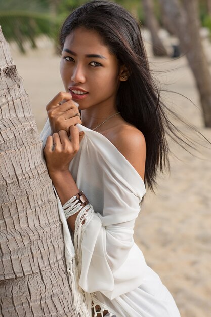 Mujer asiática en vestido blanco caminando por la playa tropical.