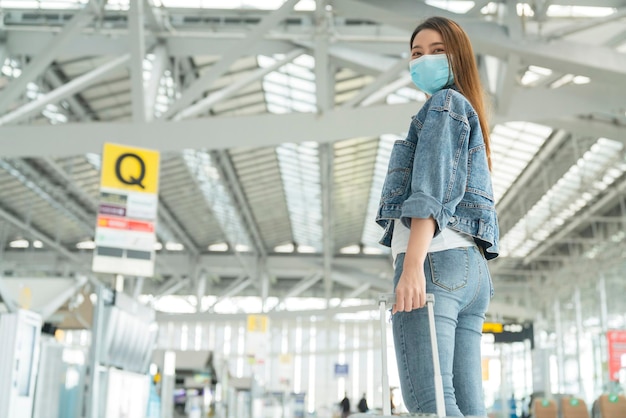 Mujer asiática viajera ropa informal usar máscara facial protección mano tirar equipaje en la terminal de salida de airoirt concepto de viaje de seguridad