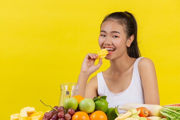 Una mujer asiática vistiendo una camiseta blanca. Yendo a comer piñas y en la mesa hay muchas frutas.