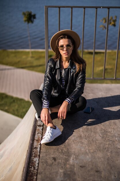 Mujer en el asiento de la chaqueta de cuero en el muelle cerca del lago en un día frío y soleado de otoño