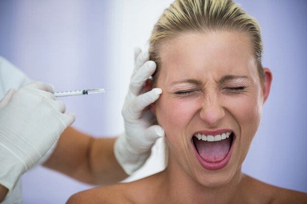 Mujer asustada gritando mientras recibe una inyección de tratamiento cosmético