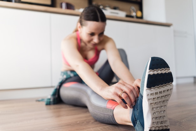 Mujer atando sus zapatos deportivos mientras está sentado en el suelo