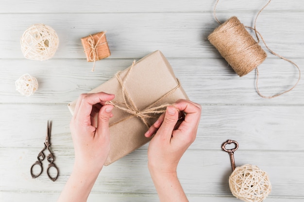 Mujer atar caja de regalo con una cuerda en superficie de madera con textura