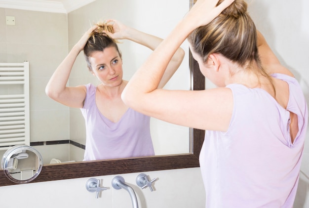 Mujer atar su cabello mirando el espejo en el baño