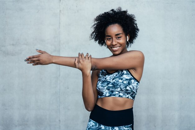 Mujer atlética afro estirando sus brazos y calentando antes de hacer ejercicio al aire libre.