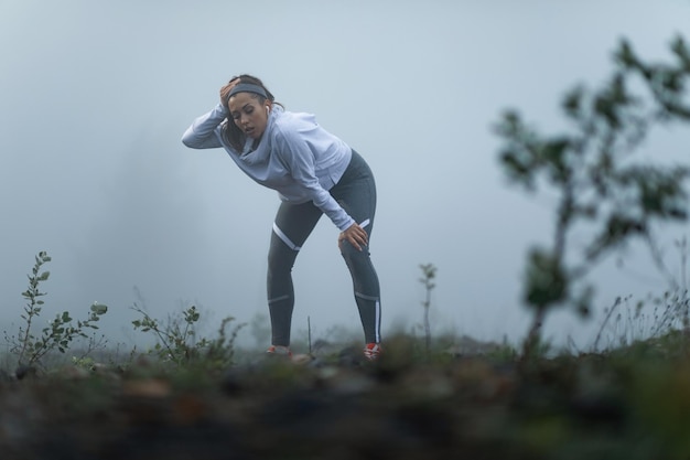 Mujer atlética cansada tomando un descanso mientras se queda sin aliento después de la carrera durante la mañana brumosa