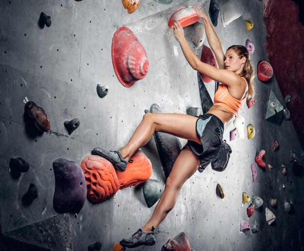 Mujer atlética escalando en un muro de escalada con efecto de luz en la imagen.