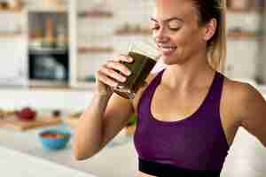 Foto gratuita mujer atlética feliz bebiendo batido verde en la cocina